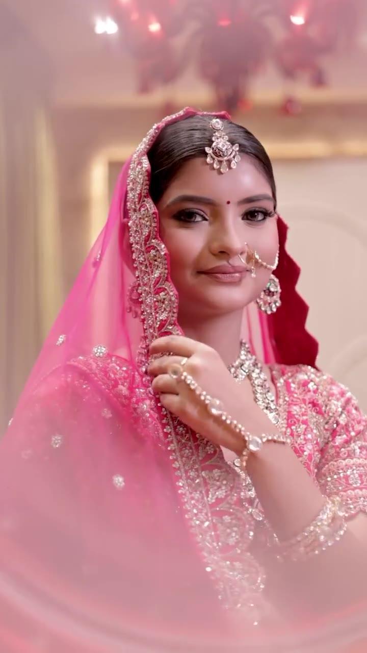 Frame from the Kapda Mandir bridal shoot video: a model in a deep pink embroidered bridal outfit with a sheer pink dupatta, a maang tikka, a nose ring and layered jewellery, looking into the camera.