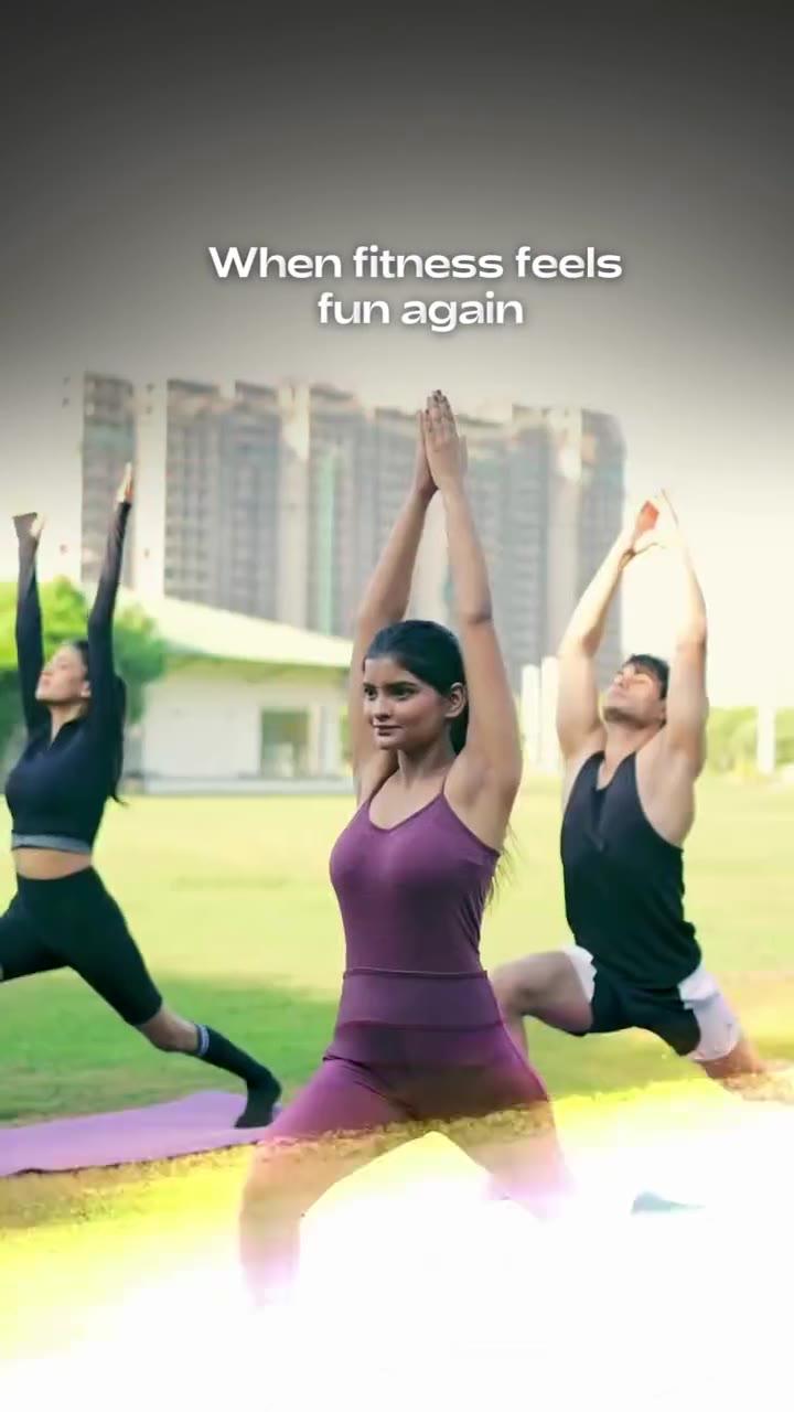 Poster frame from the Priya Living video: three people doing a yoga pose on a lawn in front of a residential building, with the on screen text When fitness feels fun again.