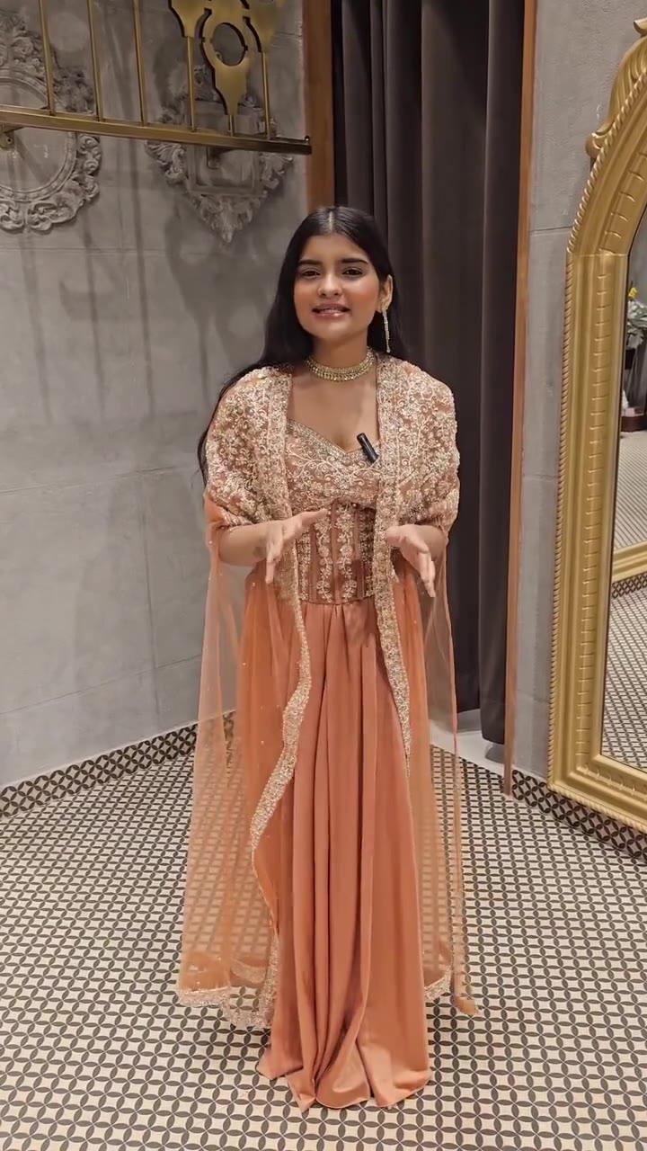 Frame from the Woman Central promo video: a woman in a peach draped outfit with an embroidered sheer cape, speaking to the camera in front of a gold framed arched mirror on a patterned tile floor.